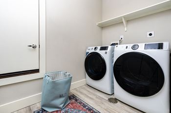 Two washing machines in a laundry room with a blue bag on the floor.